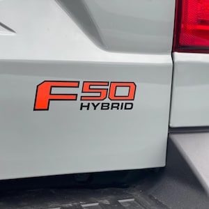 Może przedstawiać: Biały samochód dostawczy z czarno-pomarańczowym emblematem "F-50 Hybrid" z tyłu.