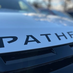 May include: A white vehicle with a black "PATHFINDER" logo on the bonnet.