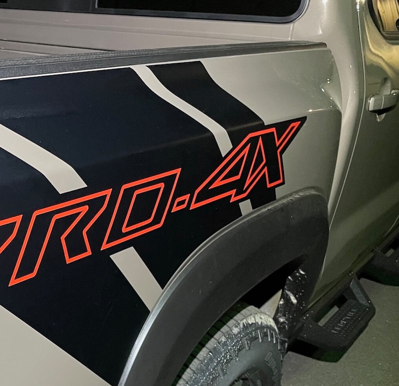 Puede incluir: Una camioneta gris con una calcoman&iacute;a de rayas blancas y negras en el lateral. La calcoman&iacute;a tiene la palabra "PRO.4X" en letras rojas.