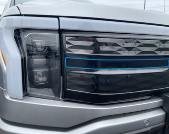 Könnte beinhalten: Nahaufnahme der Front eines silbernen Pickups mit einem schwarzen Kühlergrill. Der Kühlergrill hat ein Diamantenmuster und eine blaue Akzentlinie. Der Pickup hat schwarze Scheinwerfer.