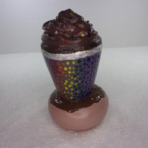 May include: A ceramic sculpture of a chocolate milkshake with whipped cream and sprinkles. The cup is decorated with a rainbow pattern and polka dots.