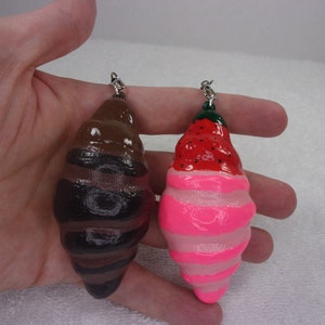 May include: Two handmade ceramic ornaments shaped like a seashell. One is painted brown and black with stripes. The other is painted pink and white with a red strawberry on top.