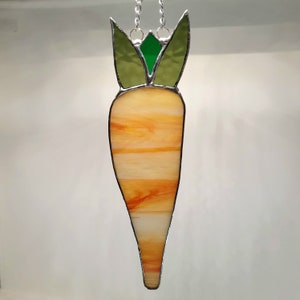 May include: A stained glass carrot hanging ornament with a green leafy top and an orange and white carrot body.