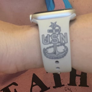 May include: White Apple Watch band with a gray anchor and the letters "USN" printed on it.
