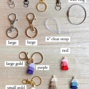 May include: Assortment of keychains and accessories in silver, black, gold, and brass. Includes a 6-inch metal wire ring and a 6-inch clear strap. Tassels in purple, red, beige, blue, and peach are also shown.