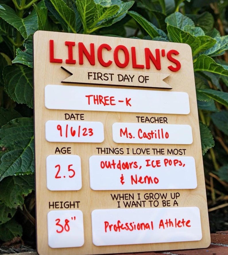 May include: A rectangular wooden sign with red and black text featuring the name LINCOLN'S, FIRST DAY OF, THREE-K, DATE 9/6/23, TEACHER Ms. Castillo, AGE 2.5, HEIGHT 38", THINGS I LOVE THE MOST outdoors, ICE POPS, & Nemo, and WHEN I GROW UP I WANT TO BE A Professional Athlete.