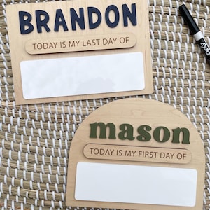 May include: Two wooden signs with white dry-erase panels. The rectangular sign features the dark blue name BRANDON and the text TODAY IS MY LAST DAY OF. The arched sign features the olive green name mason and the text TODAY IS MY FIRST DAY OF.
