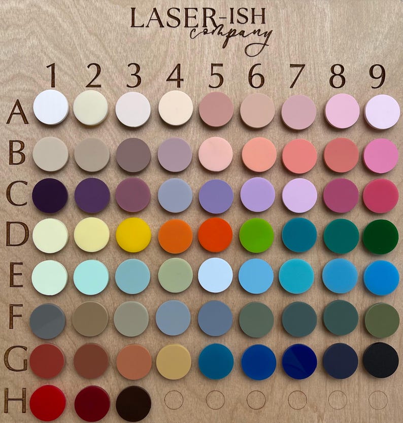 Op de afbeelding: Een kleurenkaart op een houten bord met de tekst LASER-ISH company. Het toont een raster van cirkelvormige acrylstalen gelabeld met de letters A tot en met H en de cijfers 1 tot en met 9. De stalen tonen een grote verscheidenheid aan effen kleuren, waaronder pasteltinten, heldere tinten en donkere tinten, gerangschikt in rijen en kolommen voor eenvoudige identificatie.