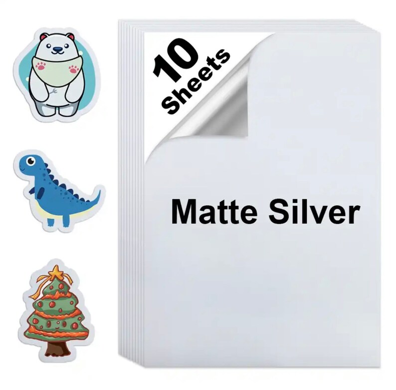 May include: A stack of ten matte silver sheets with a corner peeled back. Three stickers are visible: a polar bear, a blue dinosaur, and a Christmas tree. The text "Matte Silver" is printed on the sheets.