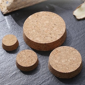 May include: Four round cork coasters of varying sizes. The coasters are made of natural cork and have a light brown colour.