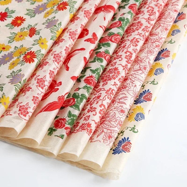 May include: A stack of patterned tissue paper sheets. The sheets feature various floral designs in red, yellow, blue, and purple on a cream background. The patterns include roses, daisies, and other stylized flowers.
