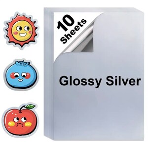 May include: A stack of 10 glossy silver sheets with the text "Glossy Silver". Three cartoon stickers of a sun, a blueberry, and an apple are on the left side of the image. The sun is yellow and red, the blueberry is blue, and the apple is red.