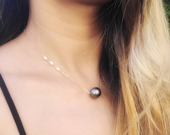 Può includere: Una delicata collana a catena dorata con una singola grande perla sferica grigio scuro come ciondolo centrale, accentuata da tre piccole perle bianche di forma ovale posizionate lungo la catena su un lato della perla principale grigio scuro.