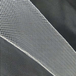 May include: White tulle fabric with a fine, diamond-shaped mesh pattern. The fabric is folded over on itself, creating a seam along the edge.
