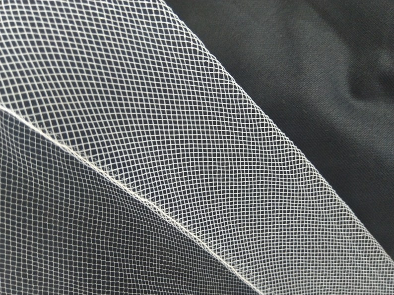 May include: White tulle fabric with a fine, diamond-shaped mesh pattern. The fabric is folded over on itself, creating a seam along the edge.