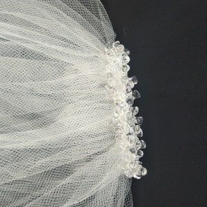 May include: White tulle bridal veil with a beaded edge. The veil is made of soft, delicate fabric and has a simple, elegant design.