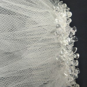 May include: White tulle fabric with a beaded trim. The trim is made of clear plastic beads.