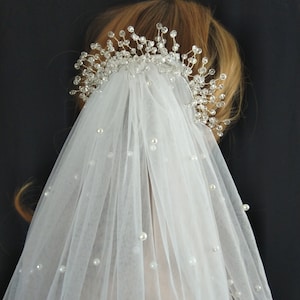 May include: A white bridal veil with pearl embellishments and a crystal and silver hair comb.