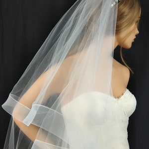 May include: A white tulle wedding veil with a single-tier design and a beaded headband. The veil has a scalloped edge and a satin ribbon trim.
