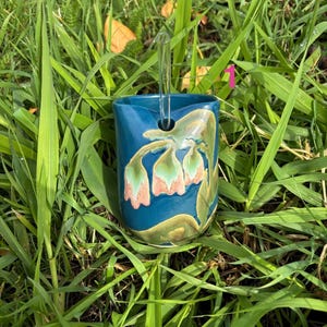 May include: A deep blue ceramic tumbler featuring a hand-painted floral design in shades of pink and green, with a clear glass straw inserted into a dedicated circular opening at the top rim, marked with the number 1 in pink text.
