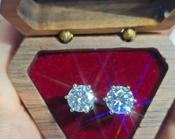 May include: A pair of sparkling diamond earrings in a wooden box with a red velvet interior. The box has the text "LEYLOON JEWELRY" on the front.