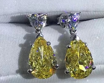 May include: A pair of silver teardrop earrings with a yellow pear-shaped stone and a smaller clear stone at the top. The earrings are on a white background.