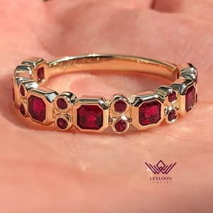 May include: A gold band ring with a row of red ruby gemstones. The ring features a mix of square and round stones.