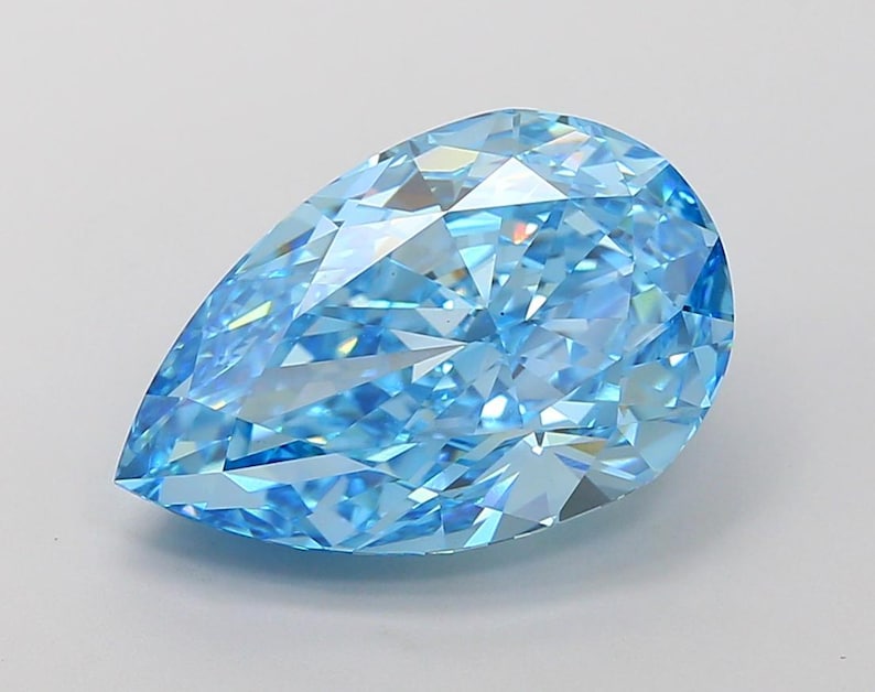 May include: A pear-shaped blue gemstone with a faceted cut. The gemstone is clear and has a light blue color.