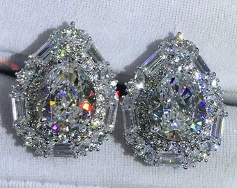 May include: A pair of pear-shaped diamond earrings with a halo setting. The earrings are set in silver and have a delicate, intricate design.