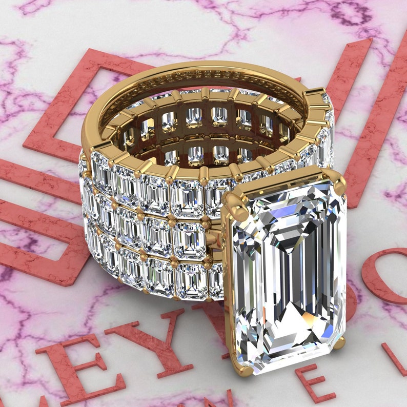 May include: A gold ring with a large emerald-cut diamond center stone and a band of smaller diamonds set in a pave setting.