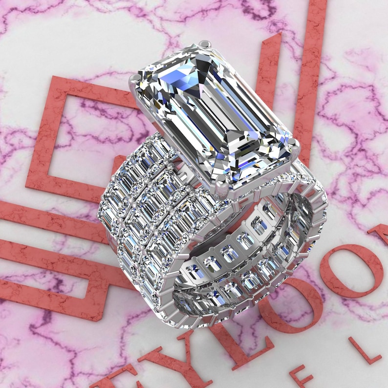 May include: A silver ring set with a large, clear emerald-cut diamond. The ring is surrounded by a band of smaller diamonds.