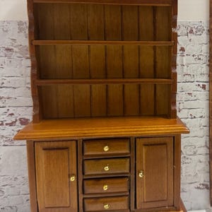 May include: A wooden hutch with a top shelf and four drawers. The hutch is brown with gold-colored knobs.