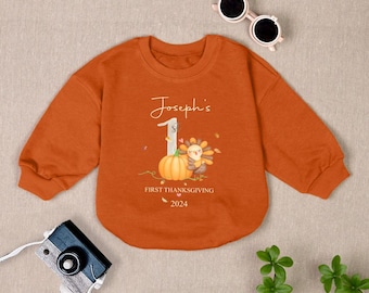 Może przedstawiać: Pomarańczowa bluza z długim rękawem z grafiką przedstawiającą dynię i indyka. Na bluzie nadrukowany jest tekst "Joseph's First Thanksgiving 2024".