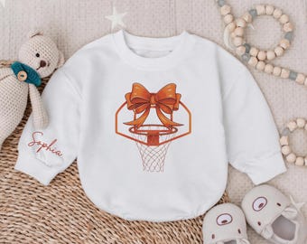 May include: White long-sleeve onesie with an orange basketball hoop and bow design. The onesie has the name "Sophia" embroidered on the sleeve.