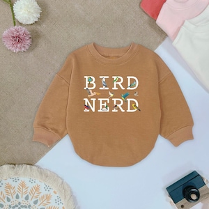 May include: A brown sweatshirt with a white graphic of the text "BIRD NERD" surrounded by colorful birds.