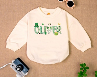 May include: A white long-sleeved shirt with a green and white checkered design. The shirt has the name "Oliver" written in green and white checkered letters with a shamrock and a leprechaun hat.