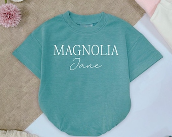 May include: A teal blue short-sleeved t-shirt with the text "Magnolia Jane" printed in white.