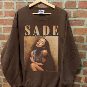 May include: Brown sweatshirt with a vintage graphic print of Sade, the singer, with the text "SADE Helen Folasade Adu CBE" on the front.