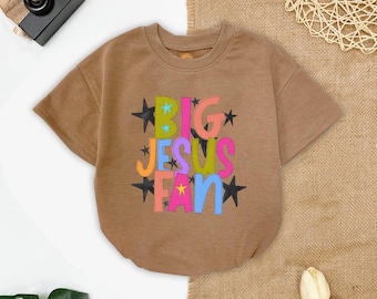 May include: A short-sleeved, brown sweatshirt with the text "BIG JESUS FAN" in colorful letters and black star accents. The shirt is made of a soft material and is suitable for casual wear.