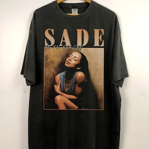 May include: Black t-shirt with a vintage-style print of Sade, a singer, with the album title "Love Deluxe" printed above her image.