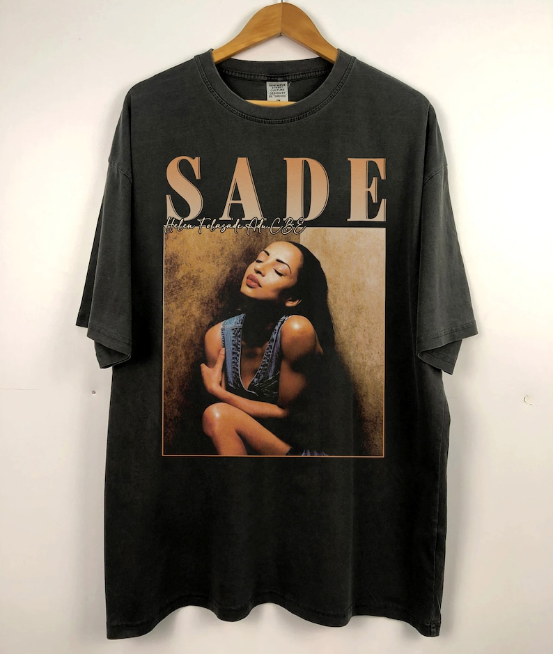 May include: Black t-shirt with a vintage-style print of Sade, a singer, with the album title "Love Deluxe" printed above her image.