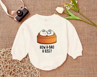 May include: White long-sleeved sweatshirt with a graphic of two cartoon bao buns in a steamer basket. The text "How a-bao a kiss?" is printed below the graphic.
