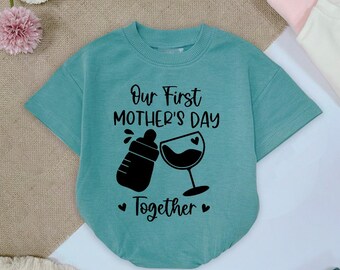 May include: A turquoise blue short-sleeved shirt with the text "Our First Mother's Day Together" printed in black. The shirt features a black graphic of a baby bottle and a wine glass.