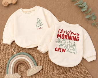 May include: Two cream-colored long-sleeve sweatshirts. One features a small green Christmas tree and the name Sophia in red. The other displays the red text Christmas Morning Crew with green illustrations of a tree, gift, stocking, and gingerbread man.
