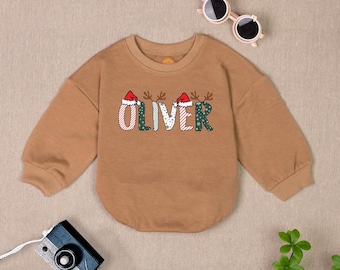 May include: A brown long-sleeved sweatshirt with a Christmas-themed design. The design features the name "Oliver" with Santa hats on each letter.