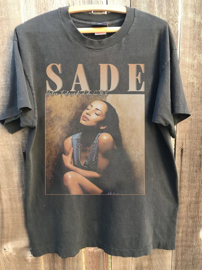 May include: A black t-shirt with a faded image of Sade, a singer, with the text "SADE Helen Folasade Adu CBE" printed on the front.