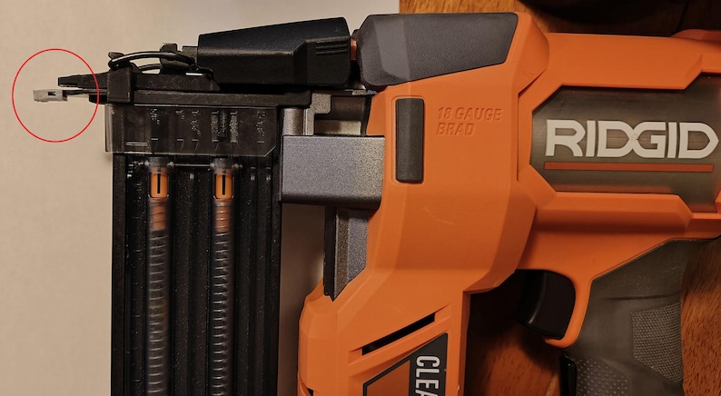 May include: An orange and black Ridgid 18-gauge brad nailer. The nailer has a black handle and a clear magazine. The text "18 GAUGE BRAD" is visible on the side. The nailer is designed for construction and woodworking projects.