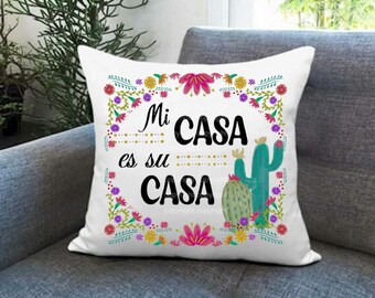 Könnte beinhalten: Ein weißes Kissen mit einem bunten Blumenrand und dem Text "Mi CASA es su CASA" in Schwarz. Das Kissen zeigt eine Illustration eines grünen Kaktus.