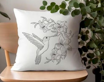 Könnte beinhalten: Ein weißes Kissen mit einer schwarz-weißen Illustration eines Kolibris, der in der Nähe einer Blumenansammlung schwebt.