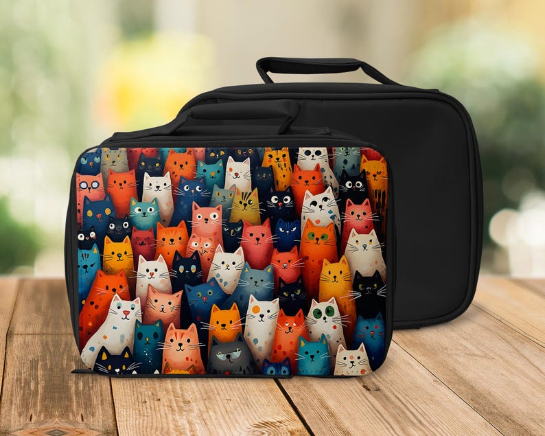 May include: Black lunch bag with a colourful cat design. The front of the bag features a vibrant illustration of numerous cats in various colours, including orange, blue, and white. The bag has a black handle and a solid black back.